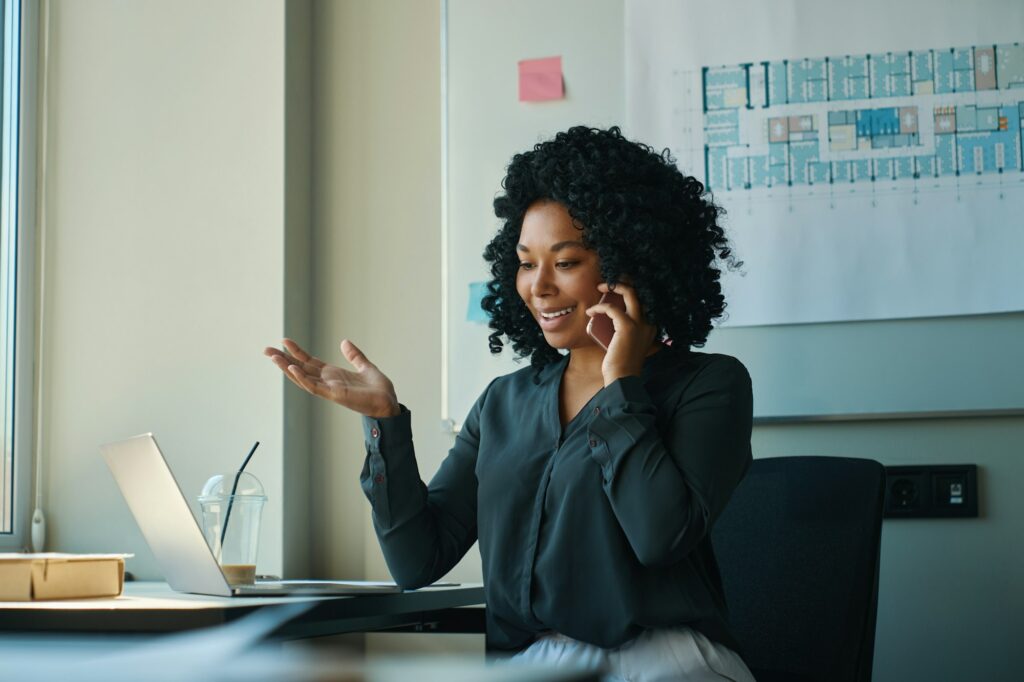 Multiracial female consults clients on the phone, uses a laptop
